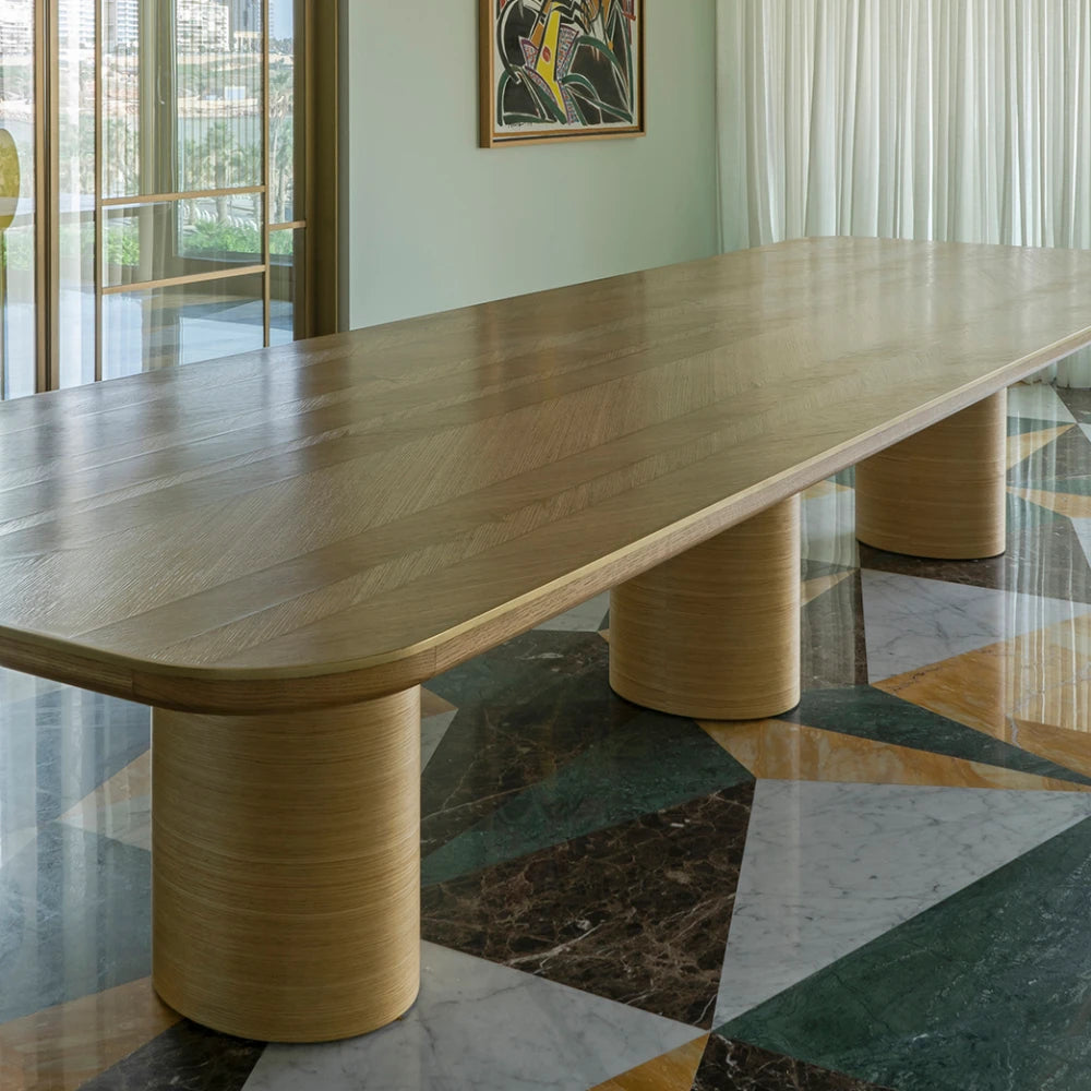 Oak DT01 Dining Table by Eva Szumilas in a bright interior, showing its long patterned wooden top and three cylindrical supports above a geometric marble floor.